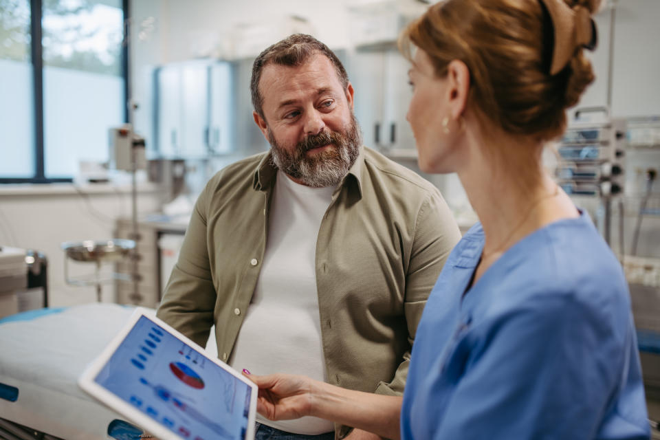 Female doctor consulting with the overweight patient, discussing test result in doctor office. Obesity affecting middle-aged men's health. Concept of health risks of overwight and obesity.