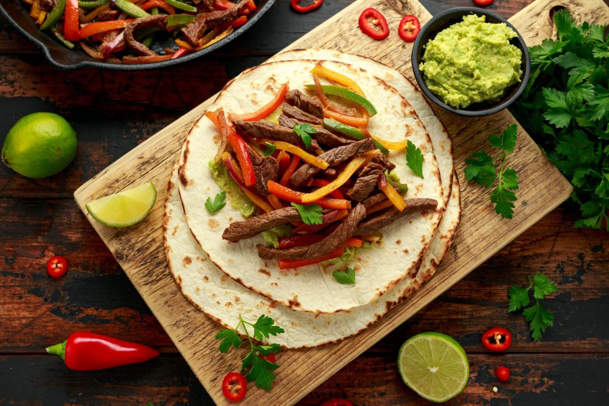 Beef Steak Fajitas with tortilla mix pepper, onion and avocado on wooden board.