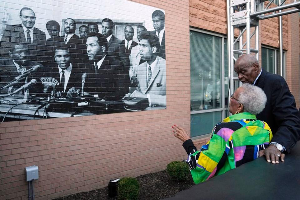 John Wooten, right, talks with Betty Pinkney, widow of Arnold Pinkney, as they look at a photo of the 1967 Cleveland summit with Muhammad Ali, Jim Brown and others, Wednesday, Oct. 11, 2023, in Cleveland. The photo is near sculptural representation of the press conference table where the Black athletes sat. (AP Photo/Sue Ogrocki)