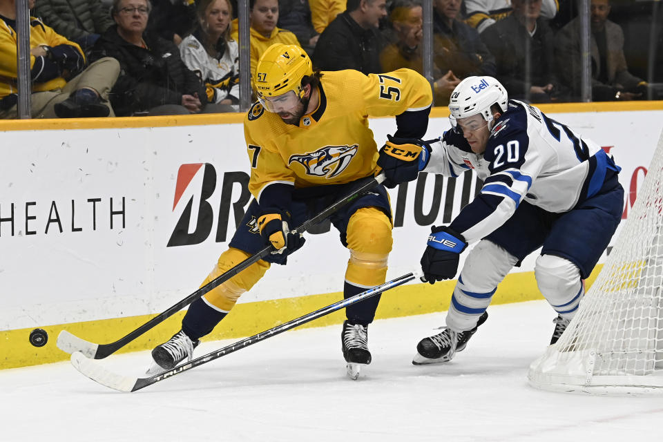 Nashville Predators defenseman Dante Fabbro (57) and Winnipeg Jets center Karson Kuhlman (20) chase the puck during the first period of an NHL hockey game Tuesday, Jan. 24, 2023, in Nashville, Tenn. (AP Photo/Mark Zaleski)