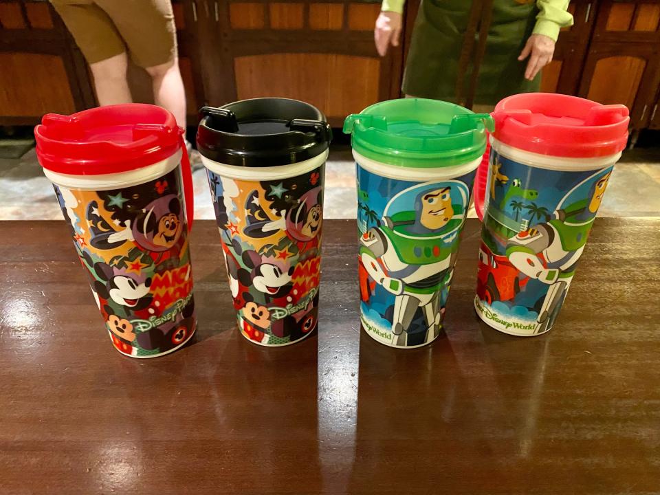 four reusable character cups from disney world in a row on a table