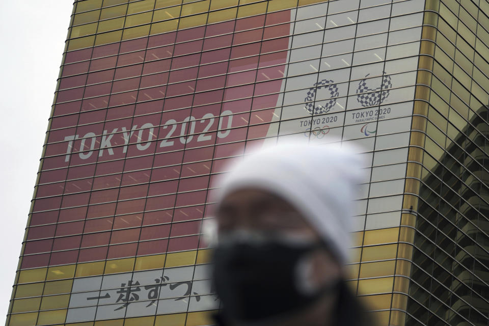 A man wearing a protective mask to help curb the spread of the coronavirus walks near a banner of the Tokyo 2020 Olympics and Paralympics Wednesday, Jan. 27, 2021, in Tokyo. (AP Photo/Eugene Hoshiko)