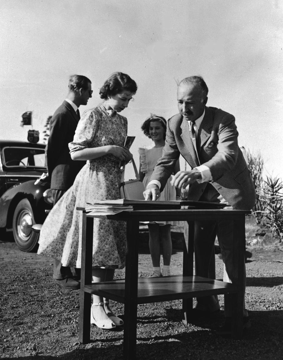 Colonel Mervyn Cowie opens the visitors book for Princess Elizabeth and the Duke Of Edinburgh to sign as they arrive at Nairobi National Park to start a car tour, Feb. 2, 1952. The royal tourists saw much of the wild life in the park, including a lion devouring his kill, some 10 yards from the car. Prince Philip is seen talking to Mitzie, daughter of Colonel Cowie. (AP Photo)