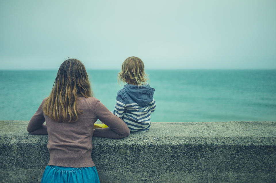 A young mother and her toddler relaxing on a wall by the sea