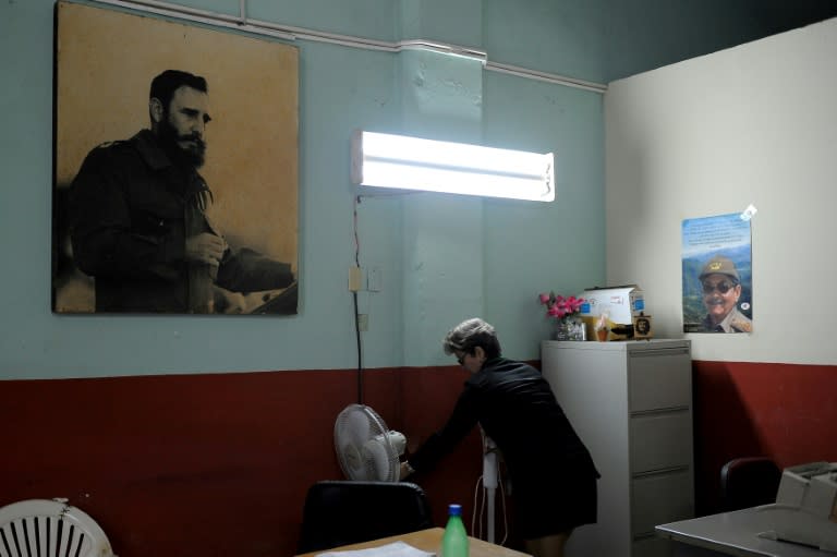 A woman works next to poster of Cuban late president Fidel Castro and Cuban president Raul Castro at her office in Havana, on February 23, 2017