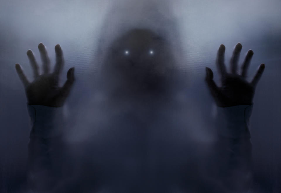 A ghostly figure with glowing eyes presses their hands against a foggy surface. The image evokes a sense of mystery and eerie intrigue