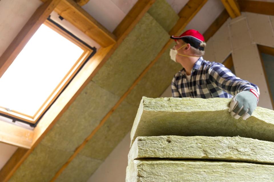 Man wearing face dust mask, insulating an attic with skylight with mineral wool.