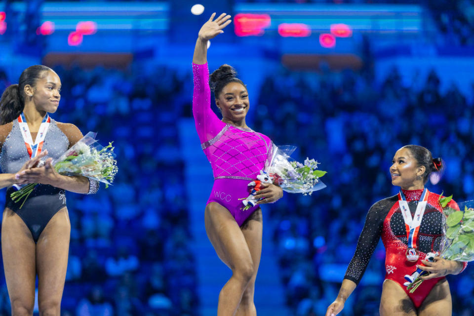 Simone Biles, Jordan Chiles, and Suni Lee stand on a podium with medals around their necks and flowers at a gymnastics competition