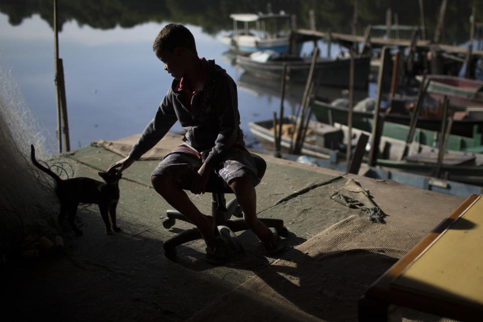 A boy plays with a stray cat during a police operation to occupy the Vila Pinheiro, part of the Mare slum complex in Rio de Janeiro, Brazil, Sunday, March 30, 2014. The Mare complex of slums, home to about 130,000 people and located near the international airport, is the latest area targeted for the government's "pacification" program, which sees officers move in, push out drug gangs and set up permanent police posts. (AP Photo/Felipe Dana)