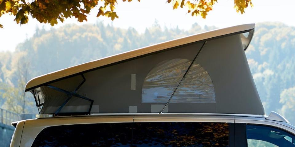 The Mercedes-Benz EQV with a pop-top roof next to a body of water surrounded by trees, nature.