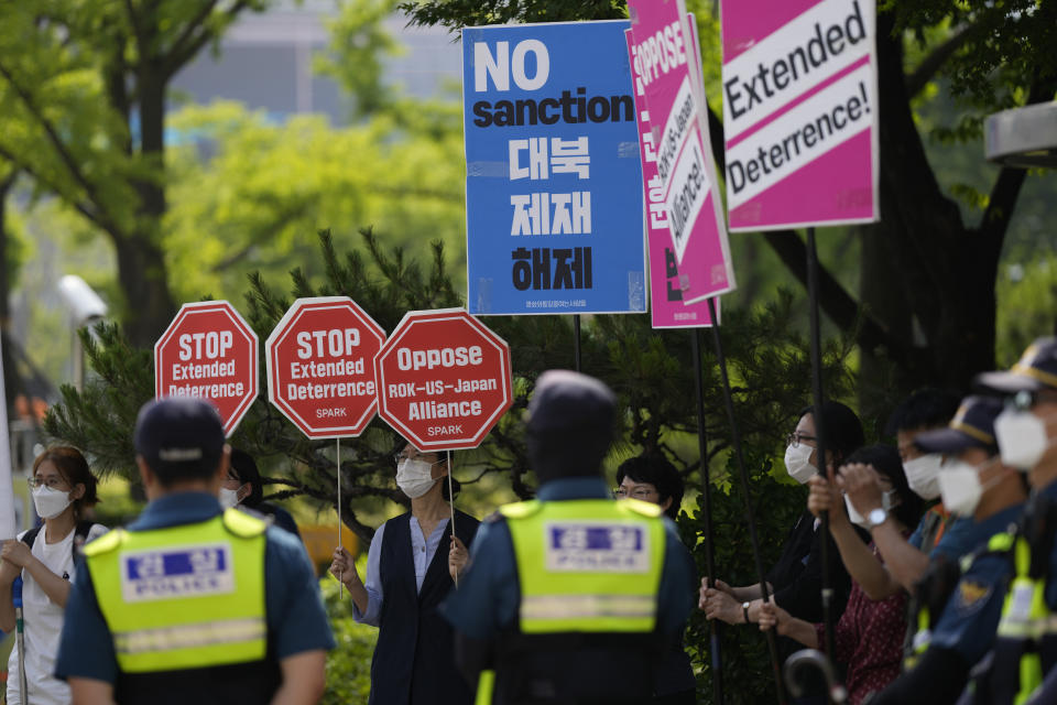 Protesters hold signs as police officers stand guard during a rally outside of Foreign Ministry where a trilateral meeting among the United States, South Korea and Japan is held in Seoul, South Korea, Friday, June 3, 2022. (AP Photo/Lee Jin-man)