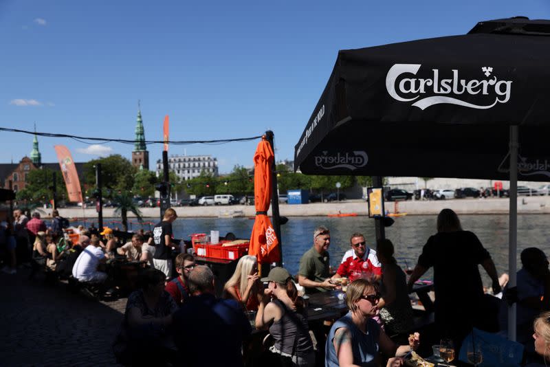 People sit under signage for Carlsberg beer in Copenhagen