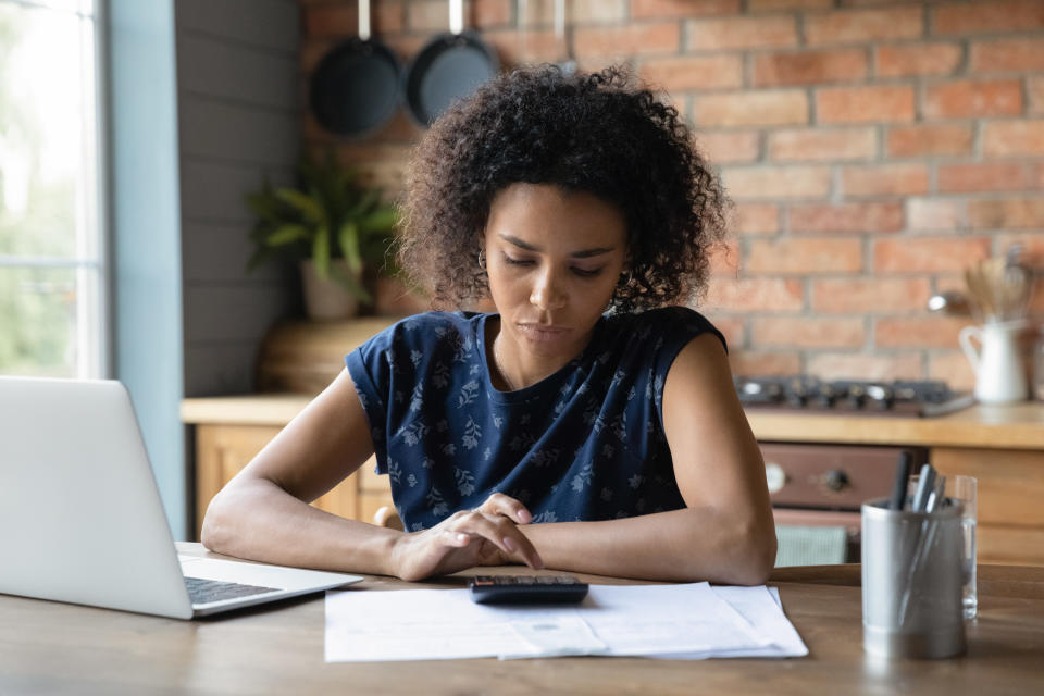 A woman sitting at a table in front of her laptop, calculator, and scattered papers