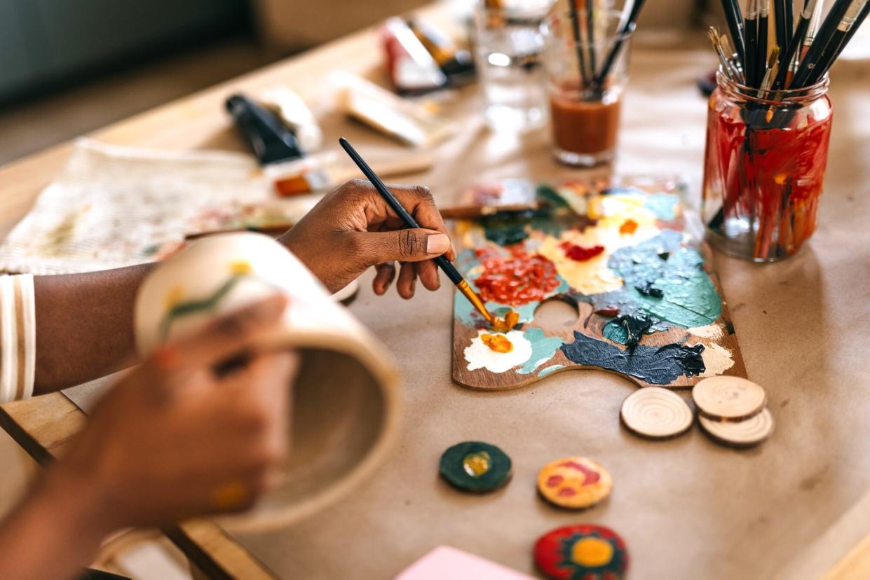 Woman painting flower pot on table at home