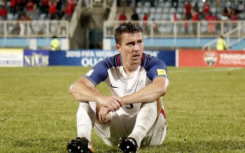 USA's Matt Besler sits on the field in dejection after losing to Trinidad and Tobago - Credit: AFP