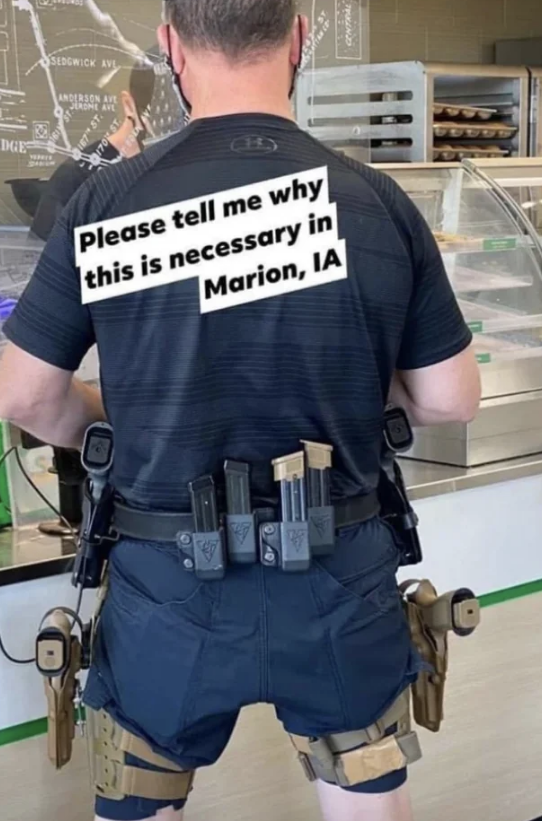 A person stands in front of a counter wearing tactical gear with guns and ammunition clips, with text over the image reading, "Please tell me why this is necessary in Marion, IA."