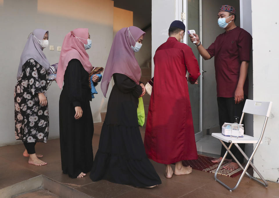 An official takes the body temperature reading of worshippers arriving for an Eid al-Adha prayer as to curb the spread of coronavirus during an Eid al-Adha prayer at Zona Madina mosque in Bogor, Indonesia,Tuesday, July 20, 2021. Muslims across Indonesia marked a grim Eid al-Adha festival for a second year Tuesday as the country struggles to cope with a devastating new wave of coronavirus cases and the government has banned large gatherings and toughened travel restrictions. (AP Photo/Tatan Syuflana)