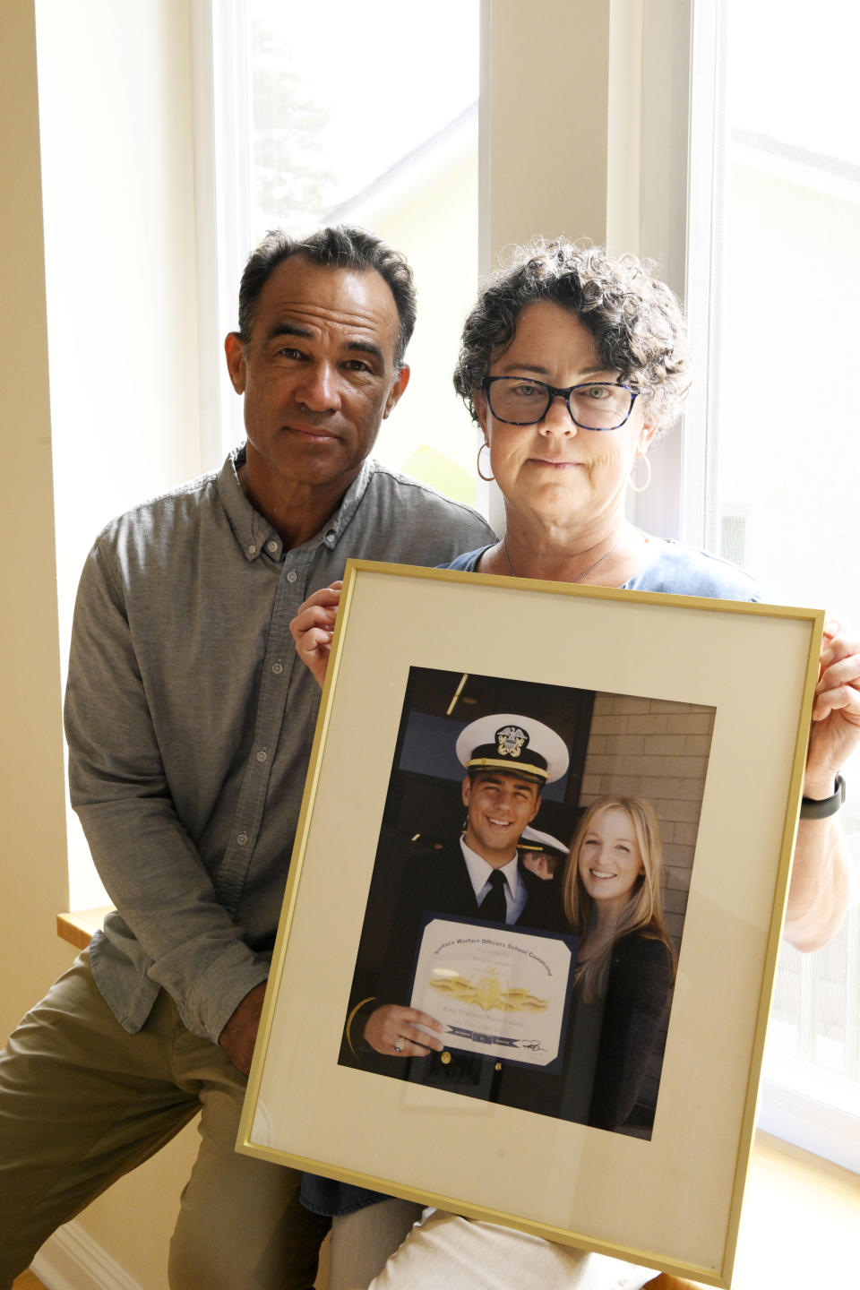 Derek and Suzi Alkonis pose with a photo of their son Lt. Ridge Alkonis and Brittany Alkonis on Wednesday, June 1, 2022, in Dana Point, Calif. Their son, a U.S. Navy lieutenant in Japan, faces a potential three-year prison sentence for a car crash that killed two people last year. The sentence has been appealed, and a hearing is set for Wednesday, June 8. (AP Photo/Denis Poroy)
