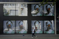 A man wearing a face mask and gloves walks past a coronavirus related artwork displayed on screens in the window of the Flannels clothing store on Oxford Street, in central London, Thursday, May 21, 2020. (AP Photo/Matt Dunham)