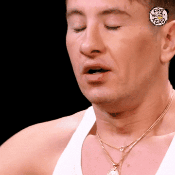 Barry Keoghan winces with eyes closed, wearing a white tank top and gold necklaces on "First We Feast."