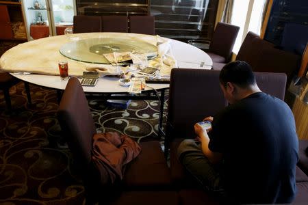 A Chinese crew member passes time by playing a game inside the banquet room of the New Imperial Star casino cruiser at Victoria Harbour in Hong Kong, China April 15, 2016. REUTERS/Bobby Yip/File Photo