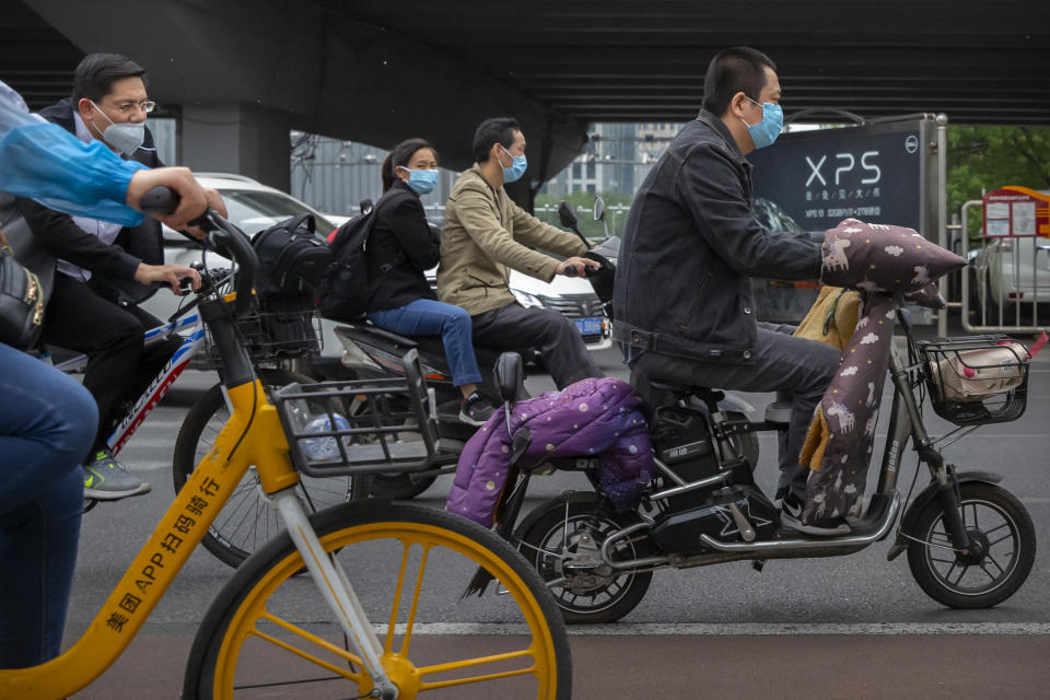 People pass by wearing face masks to protect against the spread of the new coronavirus as ride along a street in Beijing, Wednesday, May 6, 2020. China on Wednesday reported just two new cases of the coronavirus and no deaths. (AP Photo/Mark Schiefelbein)