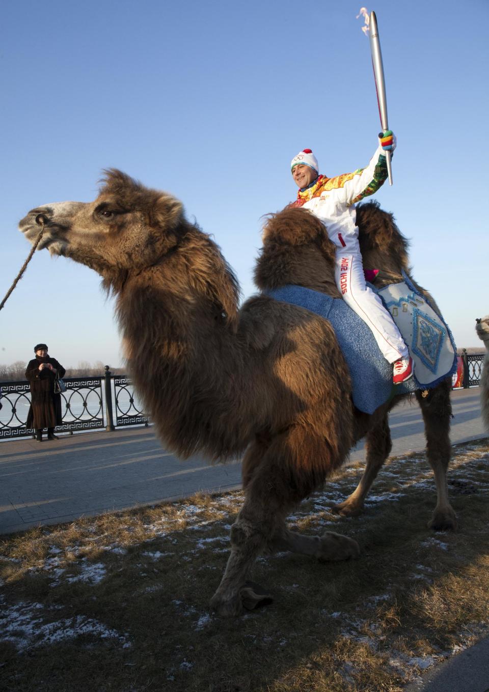 In this photo taken on Sunday, Jan. 26, 2014 and provided by Olympictorch2014.com, an Olympic torch bearer Dmitry Slaschev, top, rides a camel holding an Olympic torch during the torch relay in the southern Russian city of Astrakhan. The relay for the Sochi Winter Games, which began on Oct. 7, 2013 in Moscow, will pass through many cities that showcase the historical, cultural and ethnic richness of Russia. (AP Photo/Olympictorch2014.com)