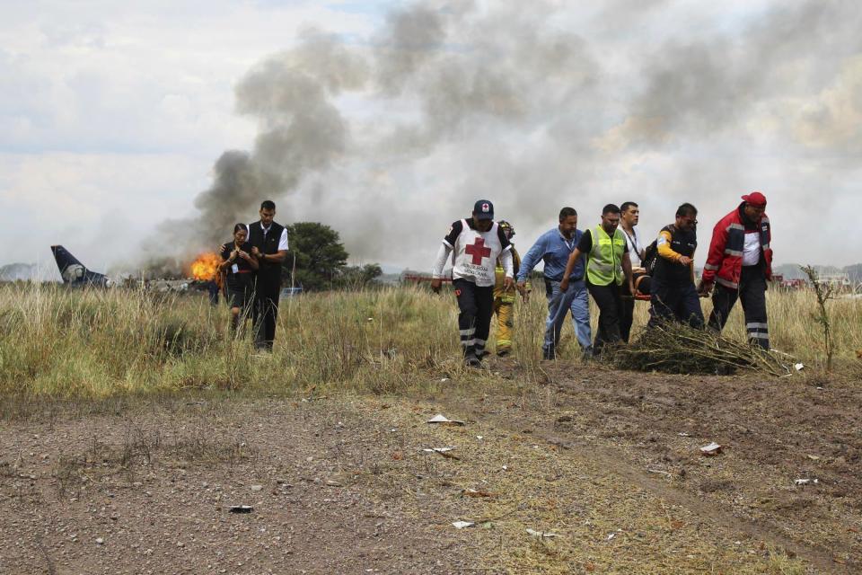 <p>In this photo released by Red Cross Durango communications office, Red Cross workers and rescue workers carry an injured person on a stretcher, right, as airline workers, left, walk away from the site where an Aeromexico airliner crashed in a field near the airport in Durango, Mexico, Tuesday, July 31, 2018. (Photo: Red Cross Durango via AP) </p>