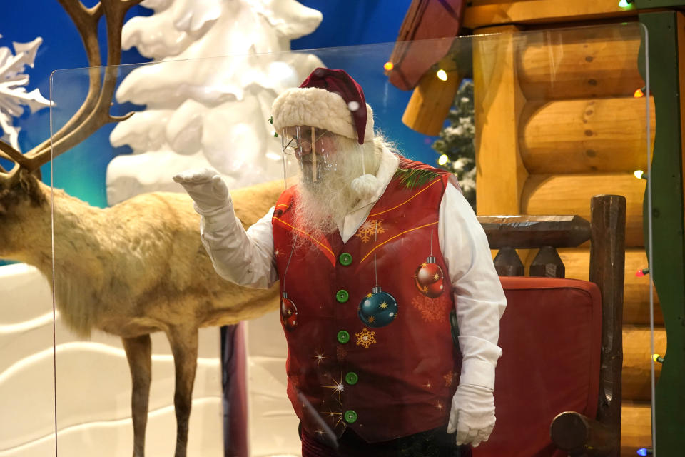 Santa Claus waves at children and their families from behind a transparent barrier at Bass Pro Shops, Friday, Nov. 20, 2020, in Miami. This is Santa Claus in the Coronavirus Age, where visits are done with layers of protection or moved online. Putting hundreds of kids a day onto your lap to talk directly into your face — that's not happening. (AP Photo/Lynne Sladky)