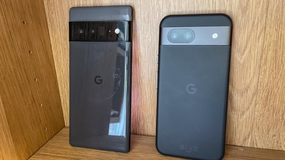 Google Pixel 8a and Google Pixel 6 Pro side by side on an oak bookshelf