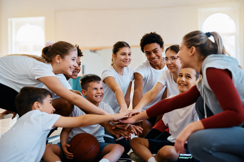 Female coach and group of students gathering their hands in unity on physical education class at school.