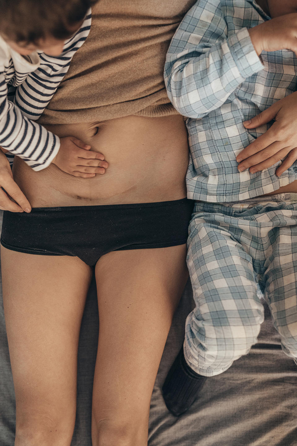 Adult and child lying close, the child touches the adult's bare pregnant belly