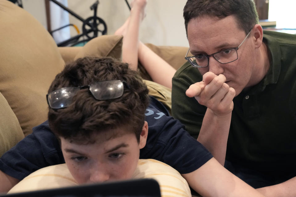 Chicago School Board candidate, former principal Adam Parrott-Sheffer, right, works with his 14 year-old son Nathan as he does his homework at their home in the Hyde Park neighborhood of Chicago, Tuesday, May 21, 2024. The nation's third-largest city is preparing for its first-ever school board elections and the slate of potential candidates include progressive activists, an afterschool squash program leader and a Grammy-winning rapper. (AP Photo/Charles Rex Arbogast)