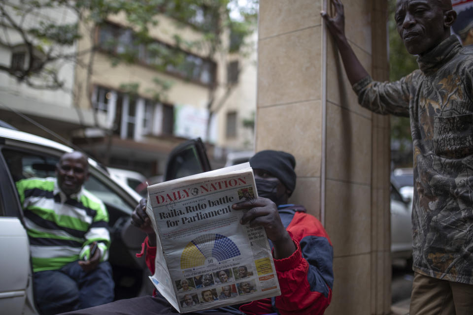 People discuss the election as a man reads a newspaper in Nairobi, Kenya, Friday, Aug. 12, 2022. Vote-tallying in Kenya's close presidential election isn't moving fast enough, the electoral commission chair said Friday, while parallel counting by local media dramatically slowed amid concerns about censorship or meddling. (AP Photo/Mosa'ab Elshamy)