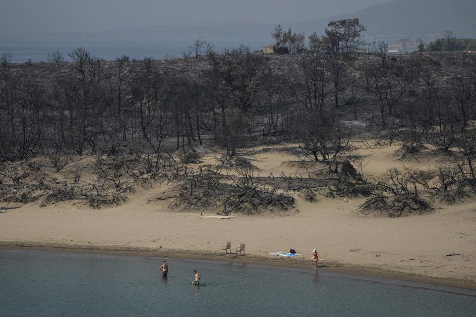 People gather on a beach in front of burnt forest near Gennadi village, on the Aegean Sea island of Rhodes, southeastern Greece, on Thursday, July 27, 2023. The wildfires have raged across parts of the country during three successive Mediterranean heat waves over two weeks, leaving five people dead. (AP Photo/Petros Giannakouris)