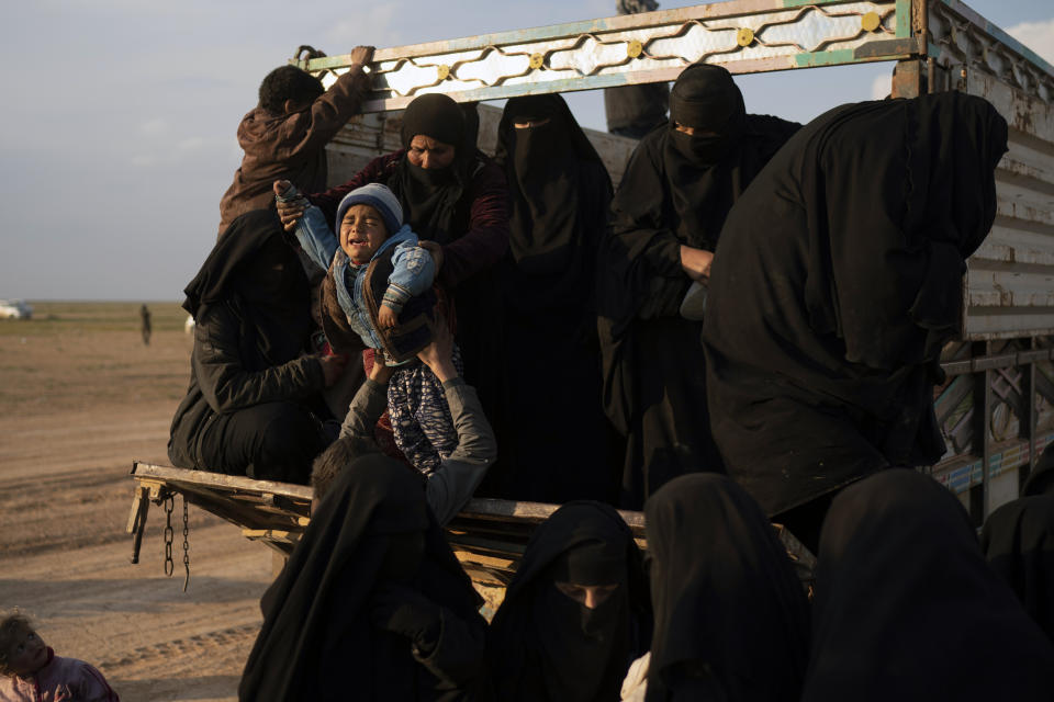 Women and children exit the back of a truck, part of a convoy evacuating hundreds out of the last territory held by Islamic State militants, in the desert near Baghouz, eastern Syria, Friday, Feb. 22, 2019. (AP Photo/Felipe Dana)