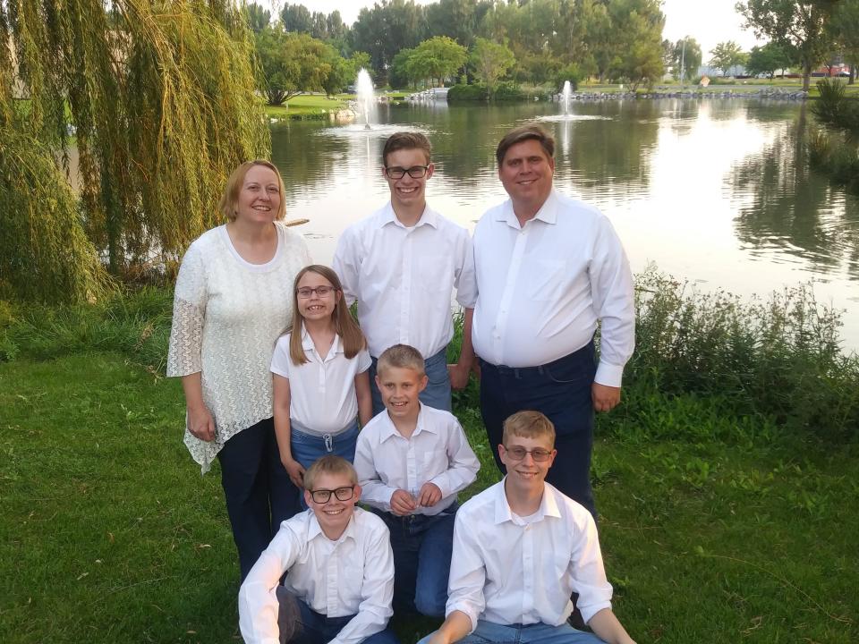 Seven members of a family pose by a lake wearing white tops and jeans