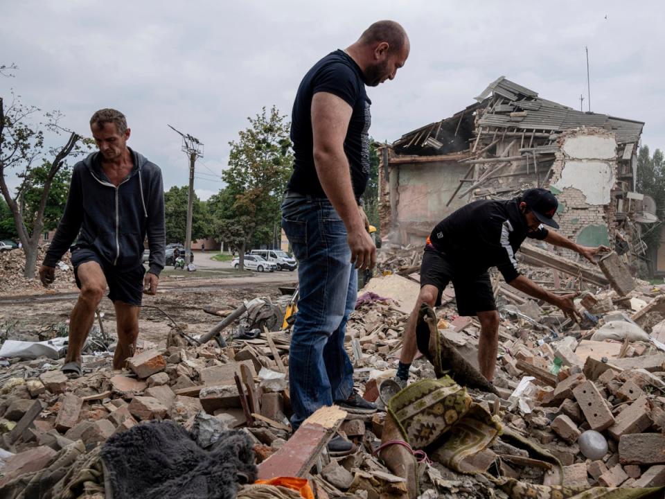 Local residents search for documents of their injured friend in the debris of a destroyed apartment house after Russian shelling in a residential area in Chuhuiv (AP)