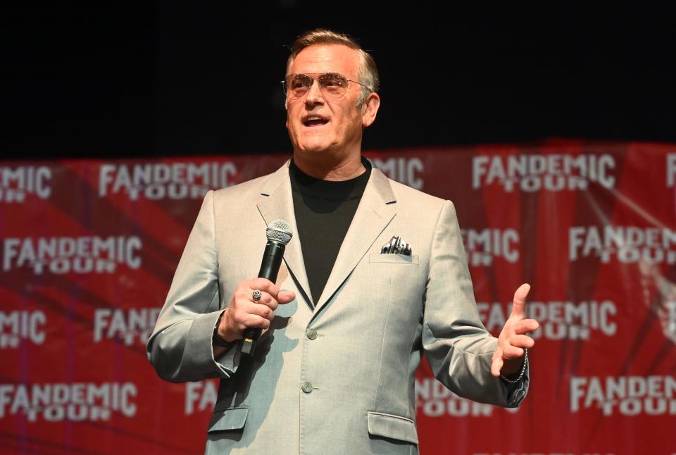 Bruce Campbell holds a microphone on stage.