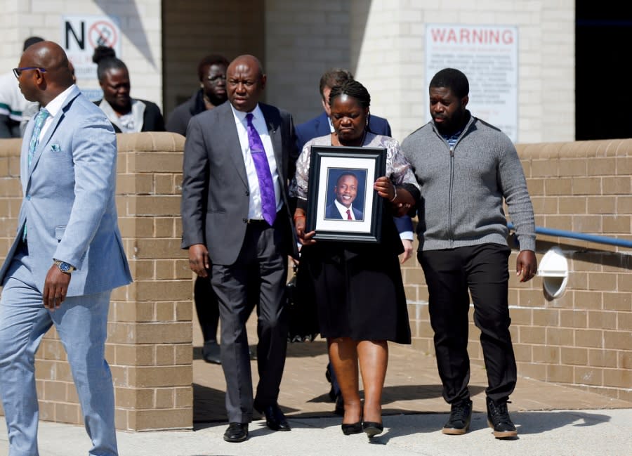 Caroline Ouko, mother of Irvo Otieno, holds a portrait of her son as she walks out of the Dinwiddie Courthouse with attorney Ben Crump, center left, and her older son, Leon Ochieng, in Dinwiddie, Va., on Thursday, March 16, 2023. Attorneys for the family of Irvo Otieno, who died in police custody say video of the incident shows seven sheriff’s deputies pushing down “every part of his body” with “absolute brutality.” (Daniel Sangjib Min/Richmond Times-Dispatch via AP)
