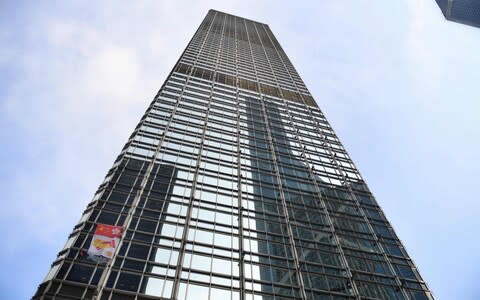 French urban climber Alain Robert, popularly known as the "French Spiderman", secures a banner, showing shaking hands below a depiction of the Chinese and Hong Kong flags - Credit: AFP