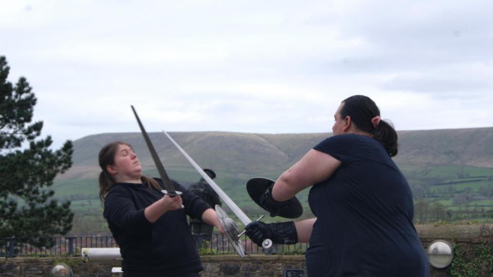 Lancashire Telegraph: Swordfighters battling at Clitheroe Castle with Pendle Hill visible in the background