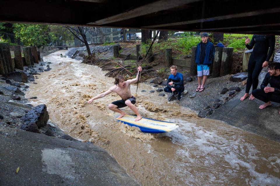 A man takes his turn using a rope from the footbridge to maintain his position and surf the rainwater.