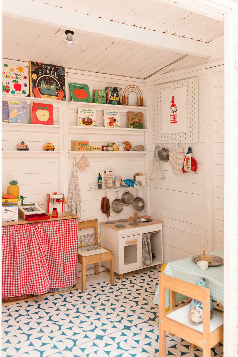 white kids' playroom with kitchen set, scale, cash register, table and chairs, and shelves with lots of books