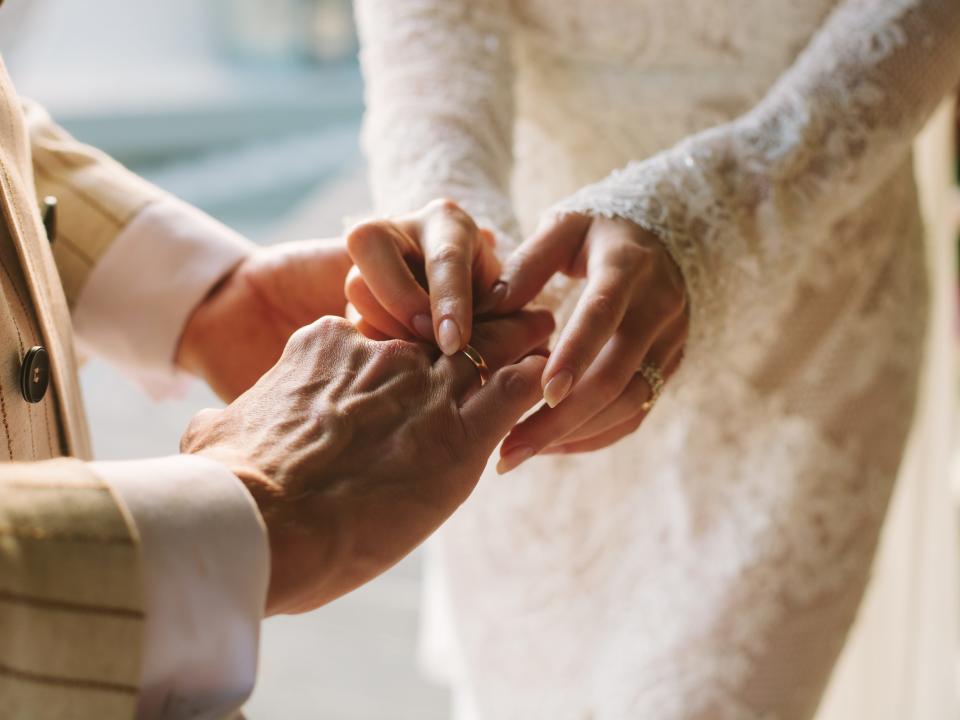 A closeup of two couples' hands exchanging wedding rings.