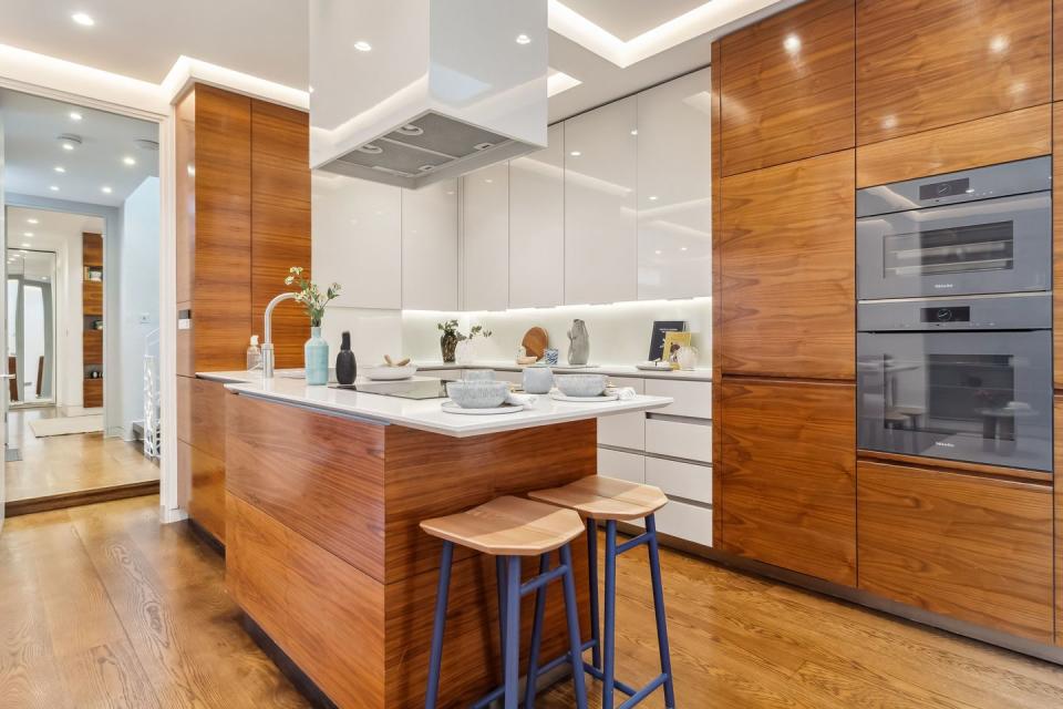 modern notting hill denbigh close kitchen with a bar island and stools with wooden and white cupboards and built in appliances