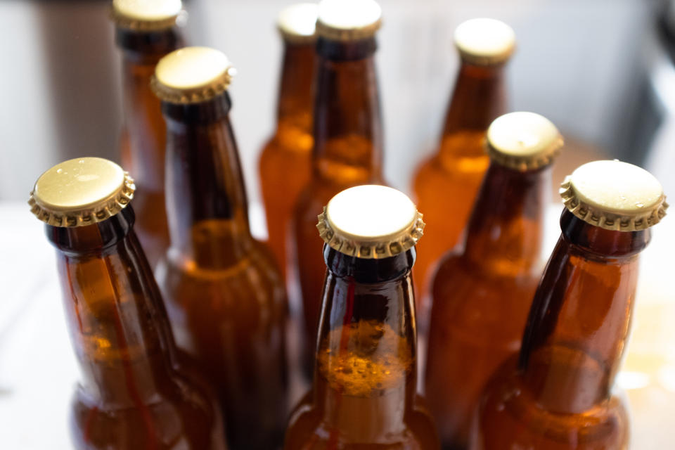 Several unopened brown beer bottles with gold caps are arranged closely together on a table