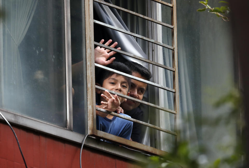 Residents wave from an apartment as Percibald Garcia reads children's books aloud outside the high-rise buildings in the Tlatelolco housing complex, in Mexico City, Saturday, July 18, 2020. Confinement during the coronavirus pandemic has been especially tedious for children, so the young architect sets out every afternoon with a microphone and a loudspeaker to walk the neighborhood where he lives and provide entertainment. (AP Photo/Marco Ugarte)