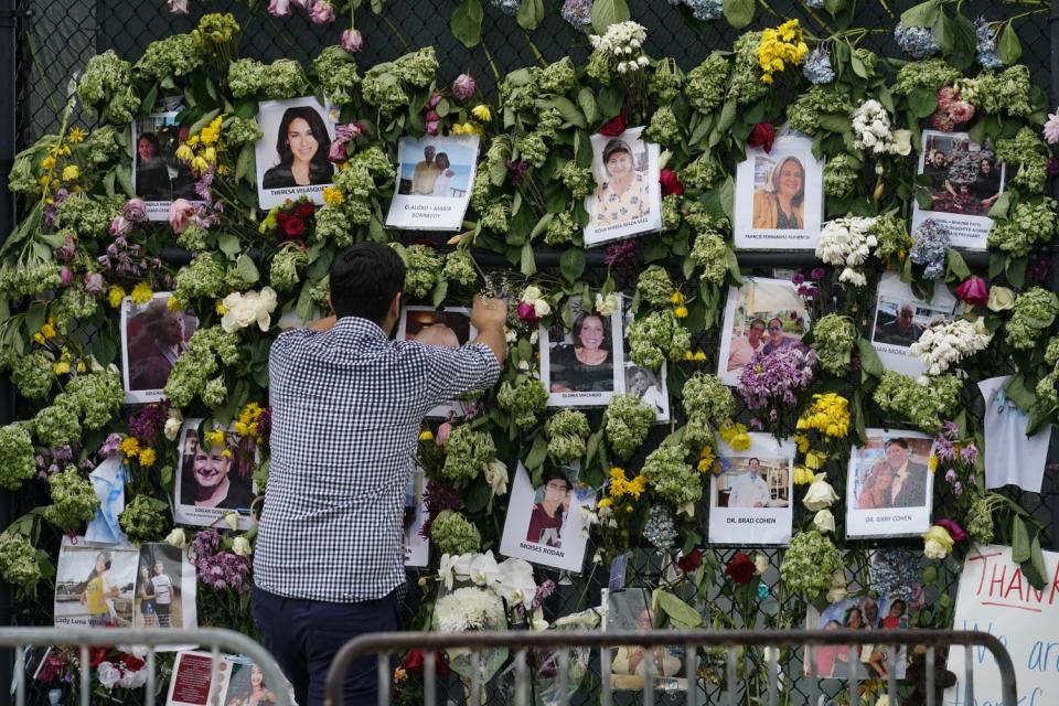 A man positions a photo pinned with others to a wall covered with flowers.