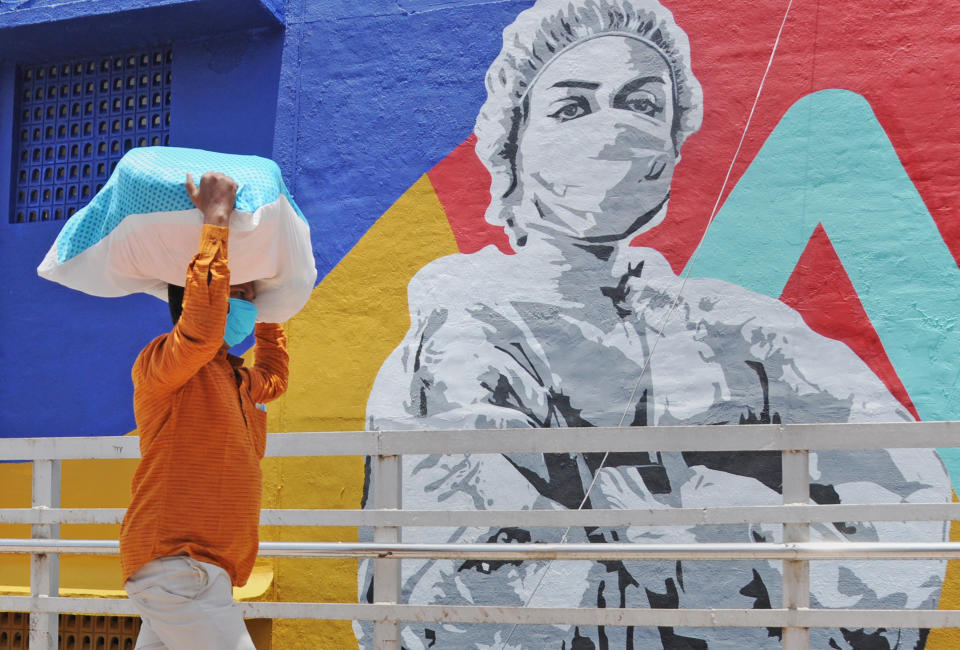 A man carrying a sack on his head walks past a graffiti of coronavirus warrior in Mumbai.Mural depicts a nurse as one of the many corona warriors who have worked throughout the lockdown, exposing themselves to the risk of infection. It is the expression of what every citizen is thankful for the efforts of essential service providers in the face of rising covid-19 cases. (Photo by Ashish Vaishnav/SOPA Images/LightRocket via Getty Images)